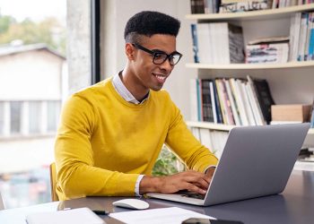 Successful african american businessman using computer at modern office. Happy creative young man feeling successful after receiving approval mail from client and working from home. Smiling student working and studying on computer sitting at desk.