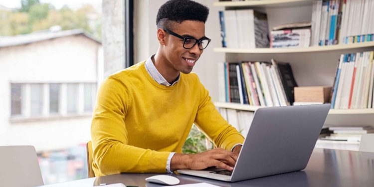 Successful african american businessman using computer at modern office. Happy creative young man feeling successful after receiving approval mail from client and working from home. Smiling student working and studying on computer sitting at desk.